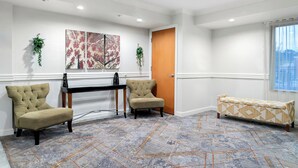 A hotel lobby with a reception desk, two armchairs, a patterned bench, and artwork on the wall. - HomeTowne Studios by Red Roof Auburn Hills (Auburn Hills)