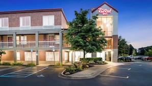 A Red Roof Inn with a two-story building, a parking lot, and a landscaped area with a tree. - HomeTowne Studios by Red Roof Auburn Hills (Auburn Hills)