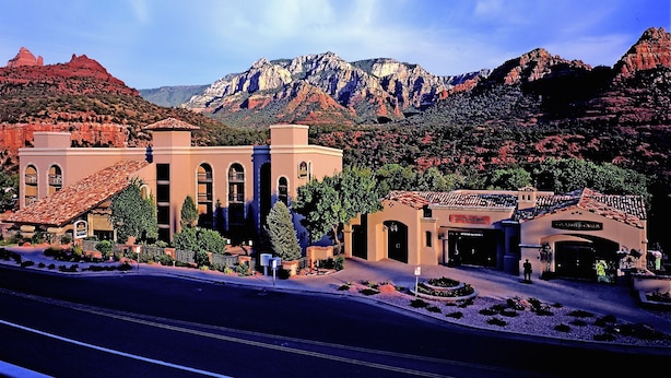 A hotel with a traditional architectural style, featuring a central courtyard, multiple entry points, and a mountainous backdrop.