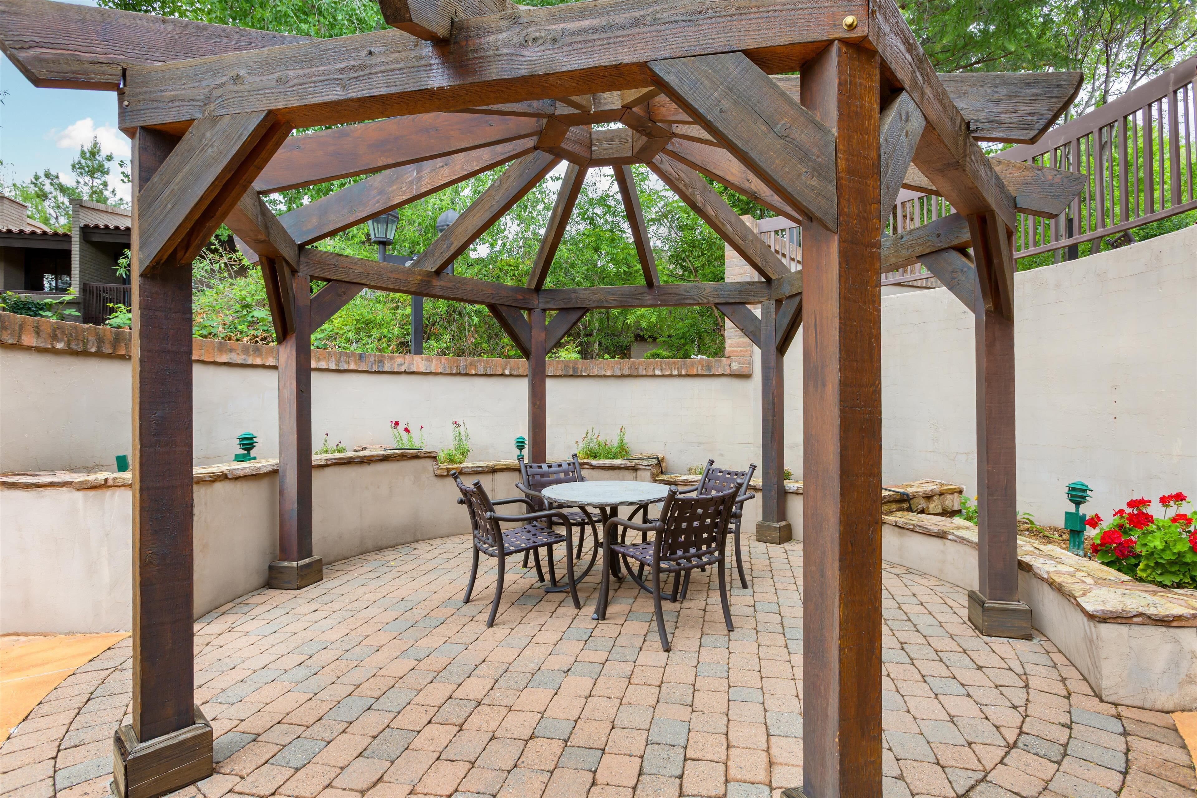 A wooden pergola with a brick patio and a round table with chairs.