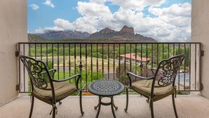 A balcony with two chairs and a table, overlooking a mountainous landscape with a clear sky.