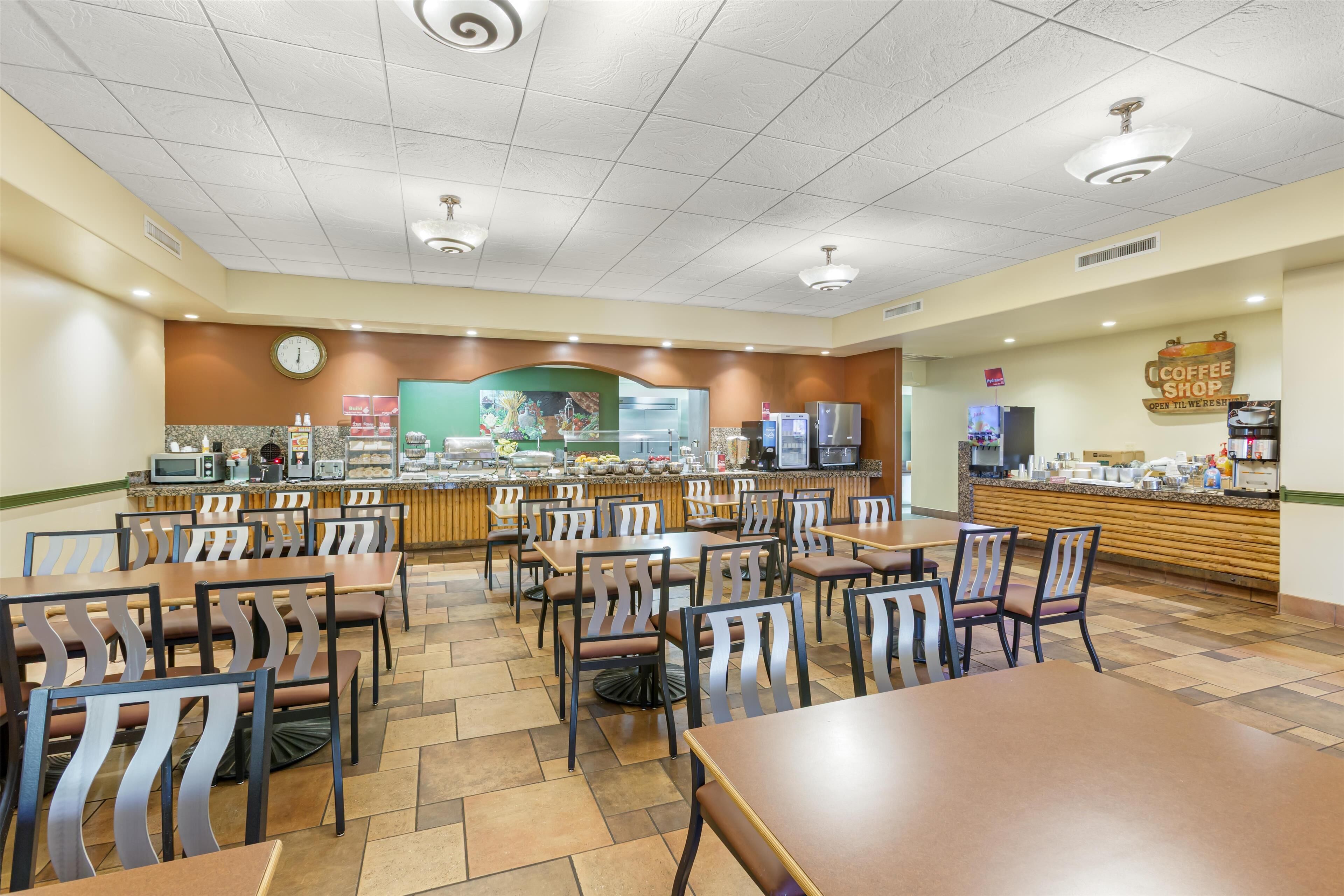 Un grand espace dédié à la restauration, avec plusieurs tables et chaises, un comptoir de café et une horloge au mur.