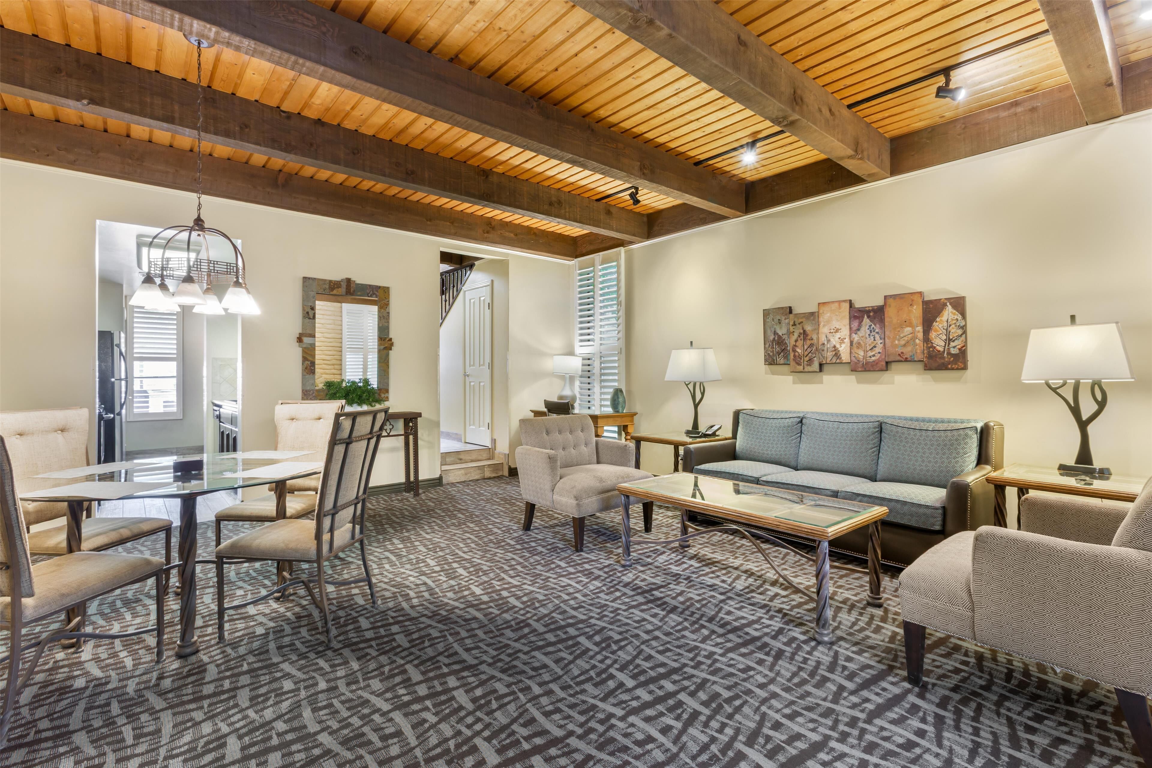 A spacious living area with a high wooden ceiling, a glass-top coffee table, a sofa, and a patterned rug.