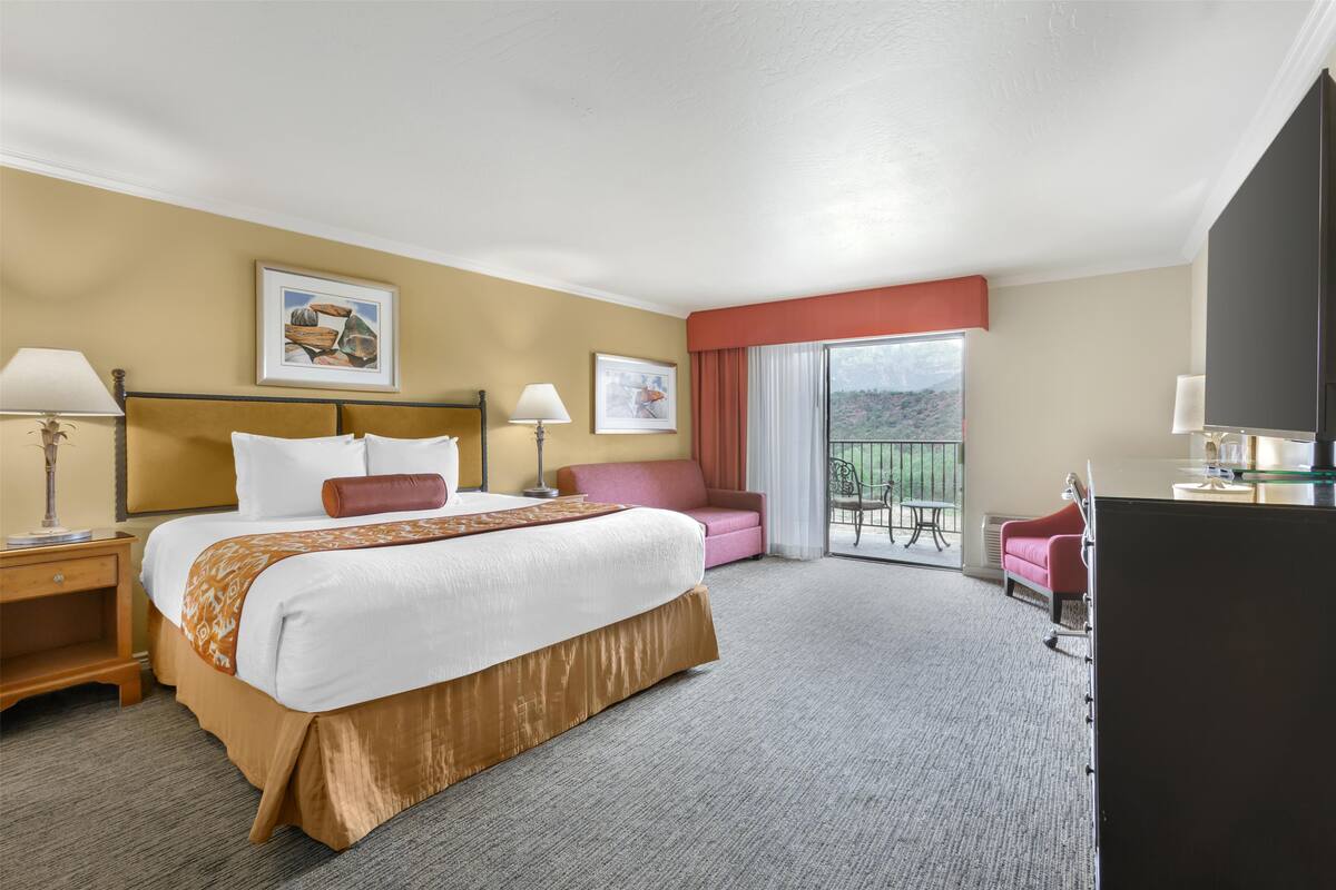 Une chambre d’hôtel avec un grand lit, un bureau, une chaise et un balcon avec vue.