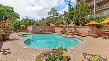 Ein Poolbereich mit Liegestühlen, Sonnenschirmen und Blumenkübeln.