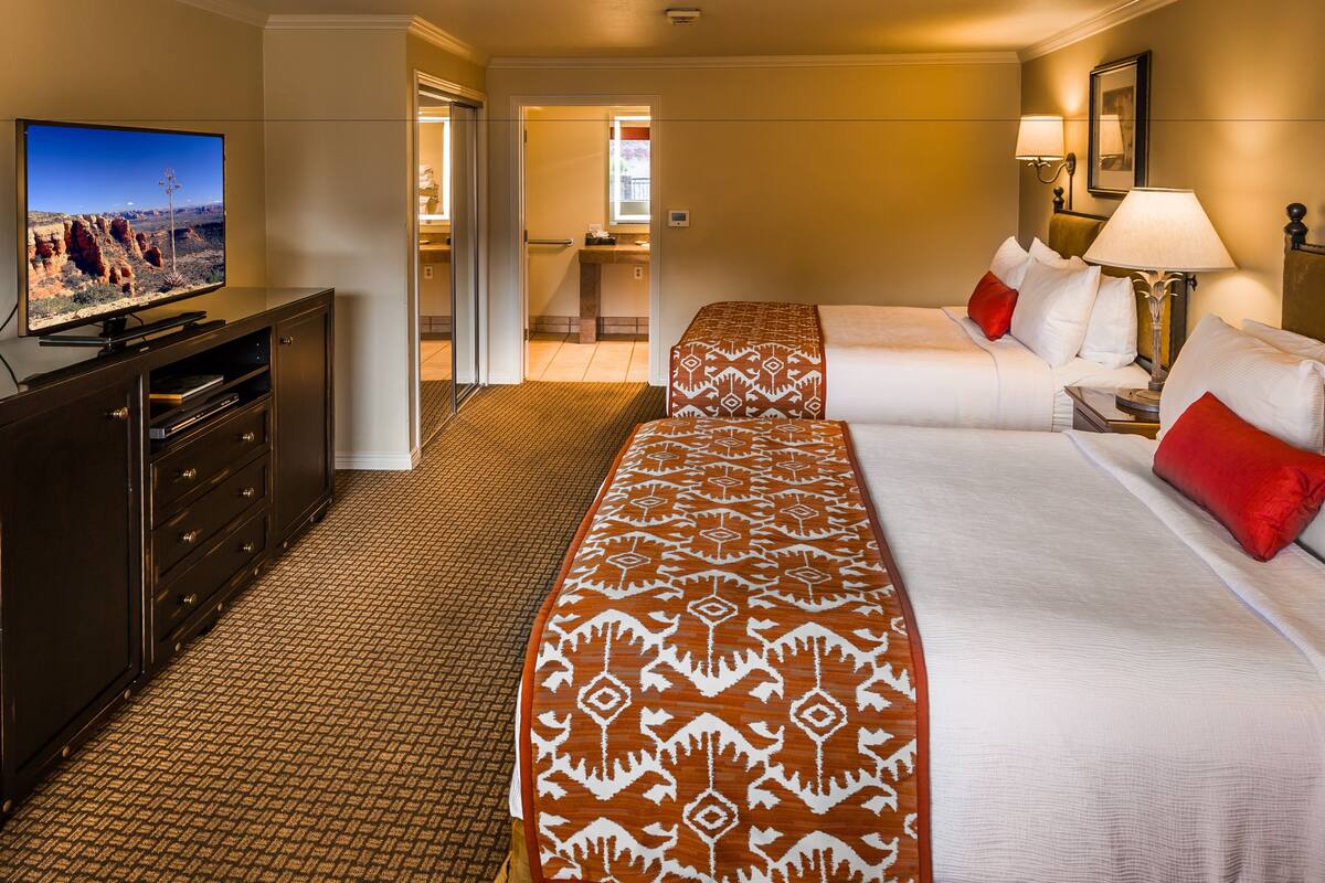 Une chambre d’hôtel avec deux lits, une télévision, un bureau et une salle de bain visible à travers une porte ouverte.