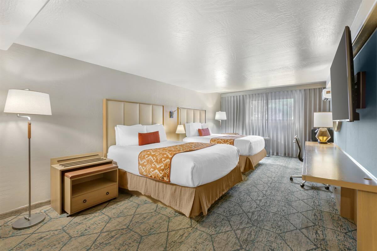 Une chambre d’hôtel avec deux lits, un bureau, un téléviseur à écran plat et une lampe sur pied.
