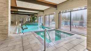 An indoor swimming pool with clear glass walls, wooden beams, and tiled flooring.