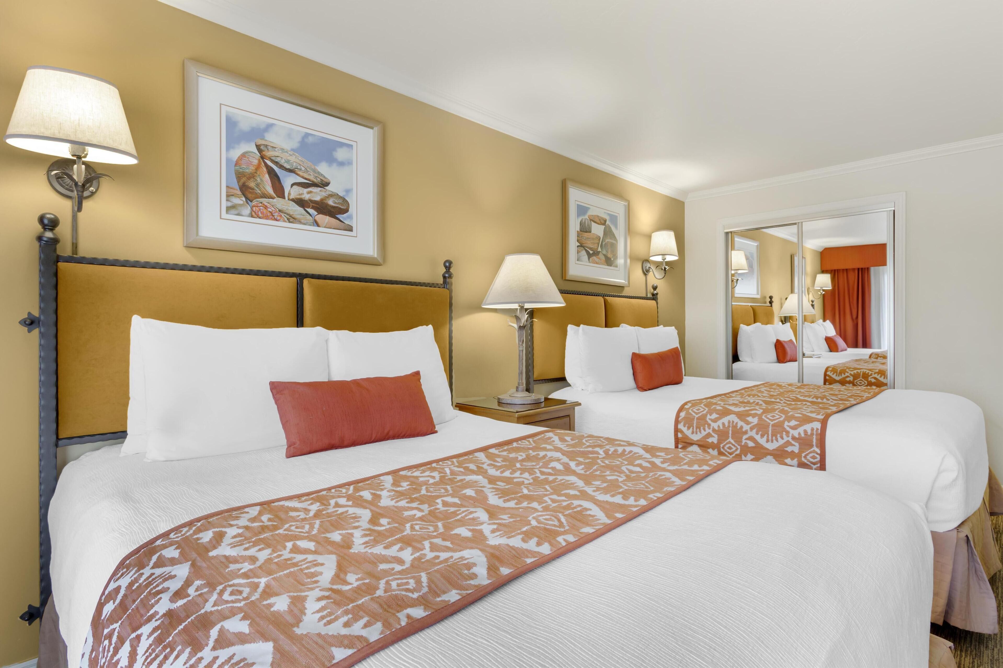 A hotel room with two beds, a large mirror, and artwork on the walls.