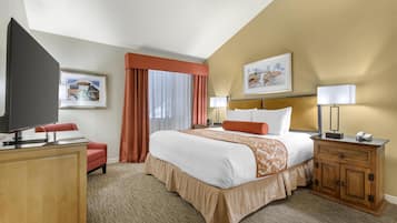 A hotel room with a bed, a TV, a desk, a chair, a nightstand, and a lamp.