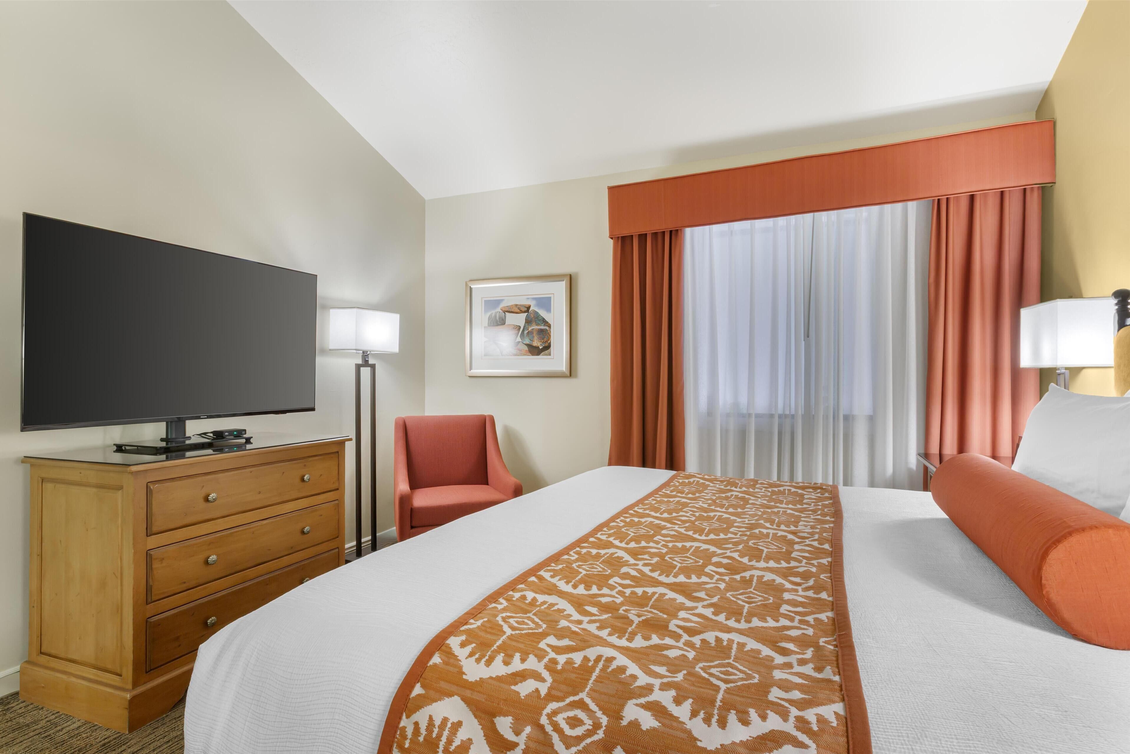 A hotel room with a large bed, a television on a wooden dresser, a chair, and a window with curtains.