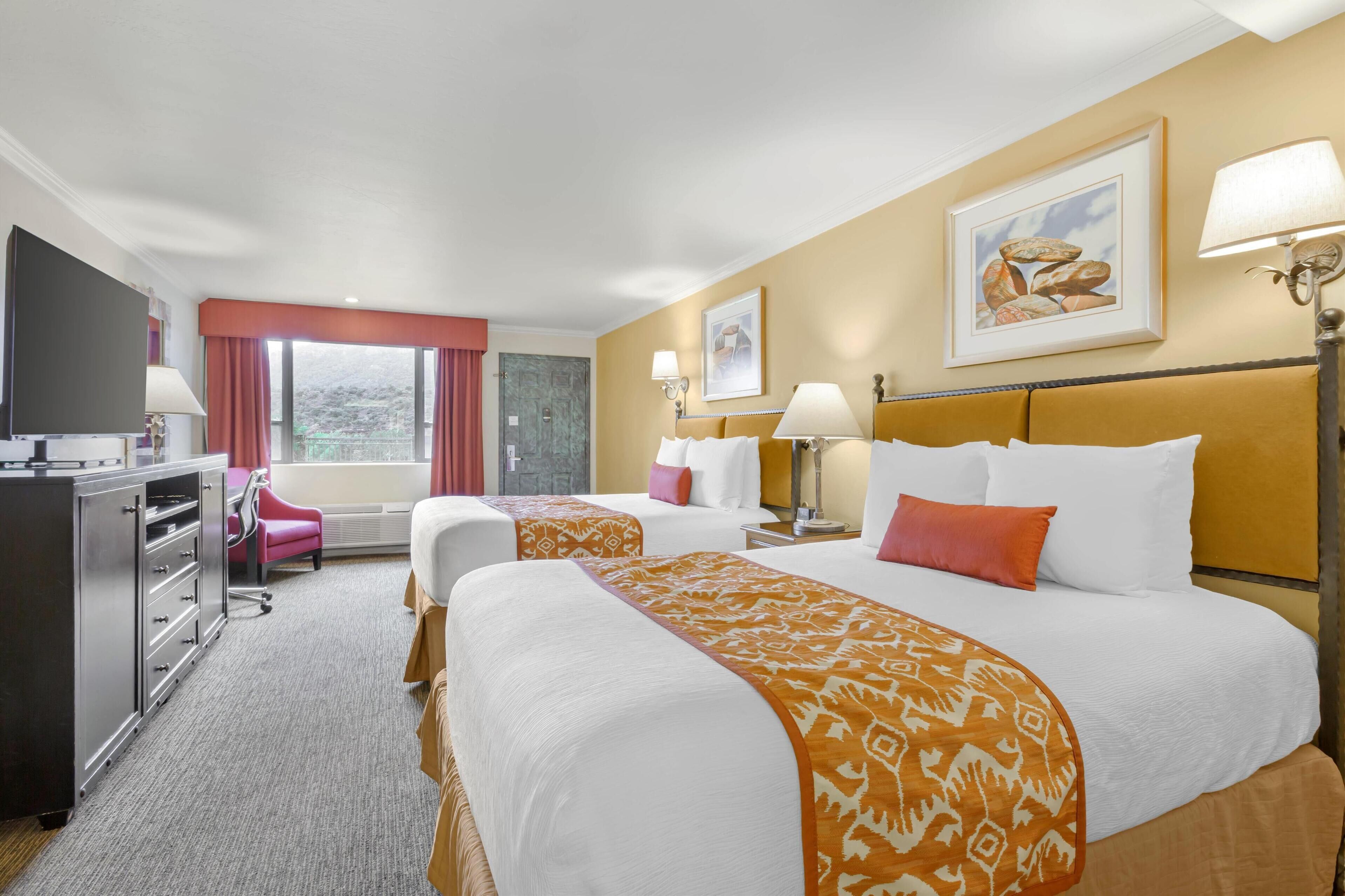 A hotel room with two beds, a desk, a chair, and a television.
