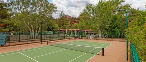 An outdoor tennis court with a net, surrounded by trees and a mountain in the background.