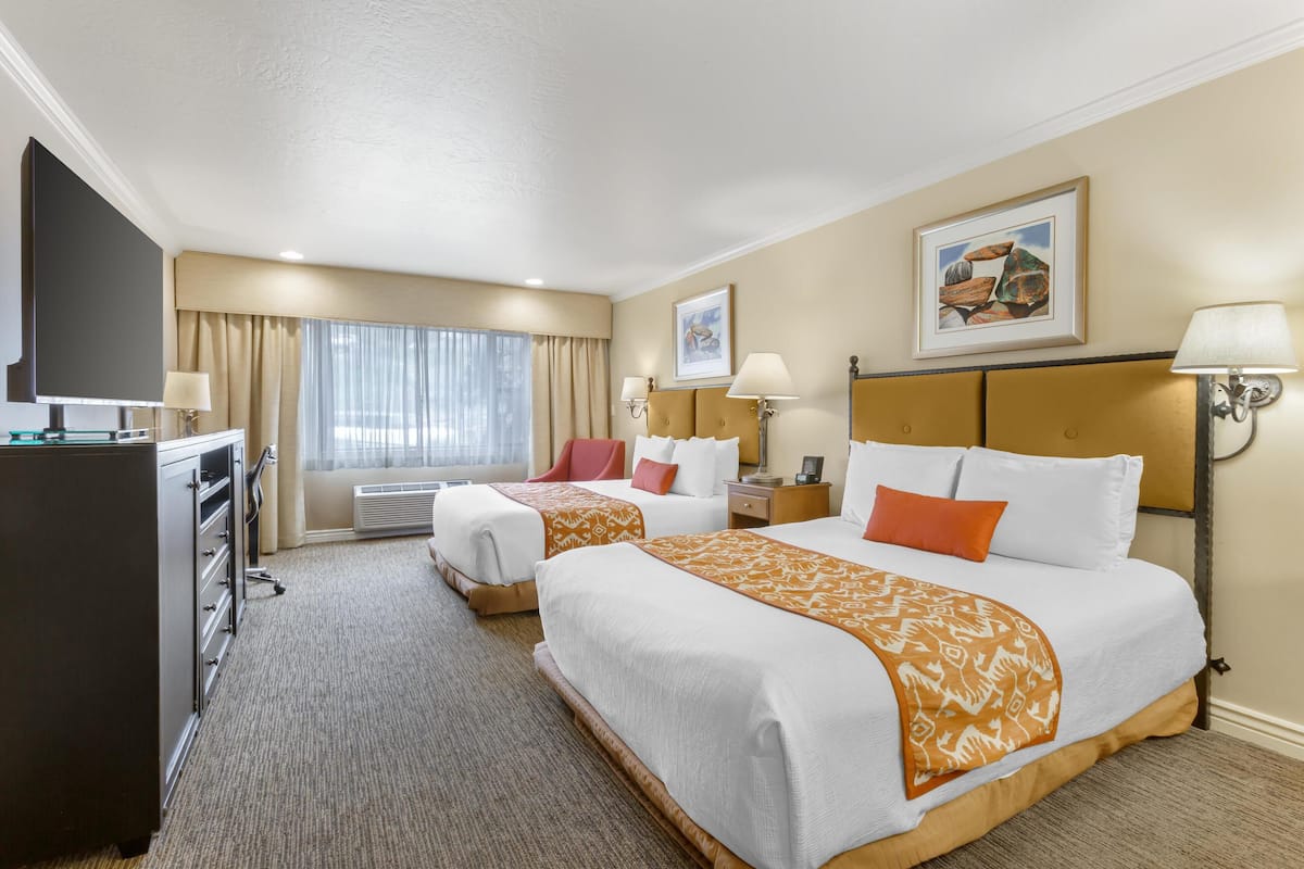Une chambre d’hôtel avec deux lits, un bureau, un téléviseur à écran plat et une grande fenêtre avec des rideaux.