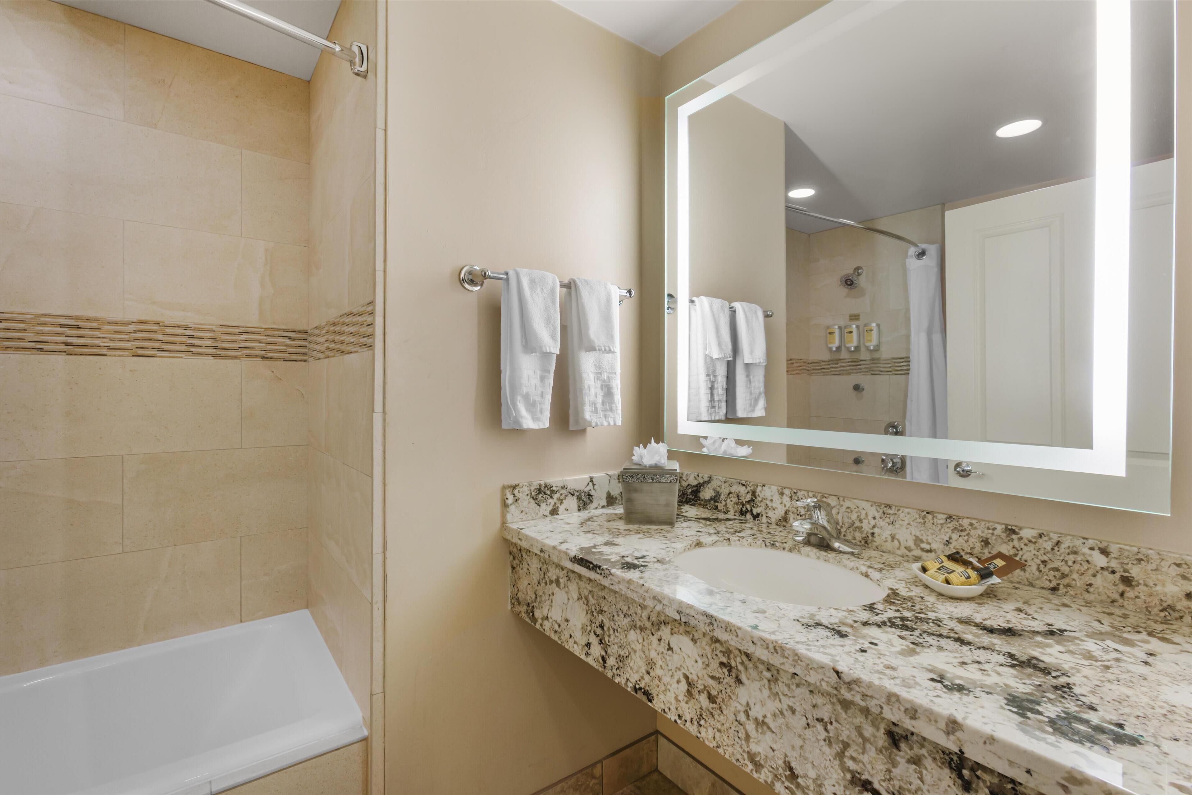A bathroom with a bathtub, a sink with a marble countertop, and a large mirror.