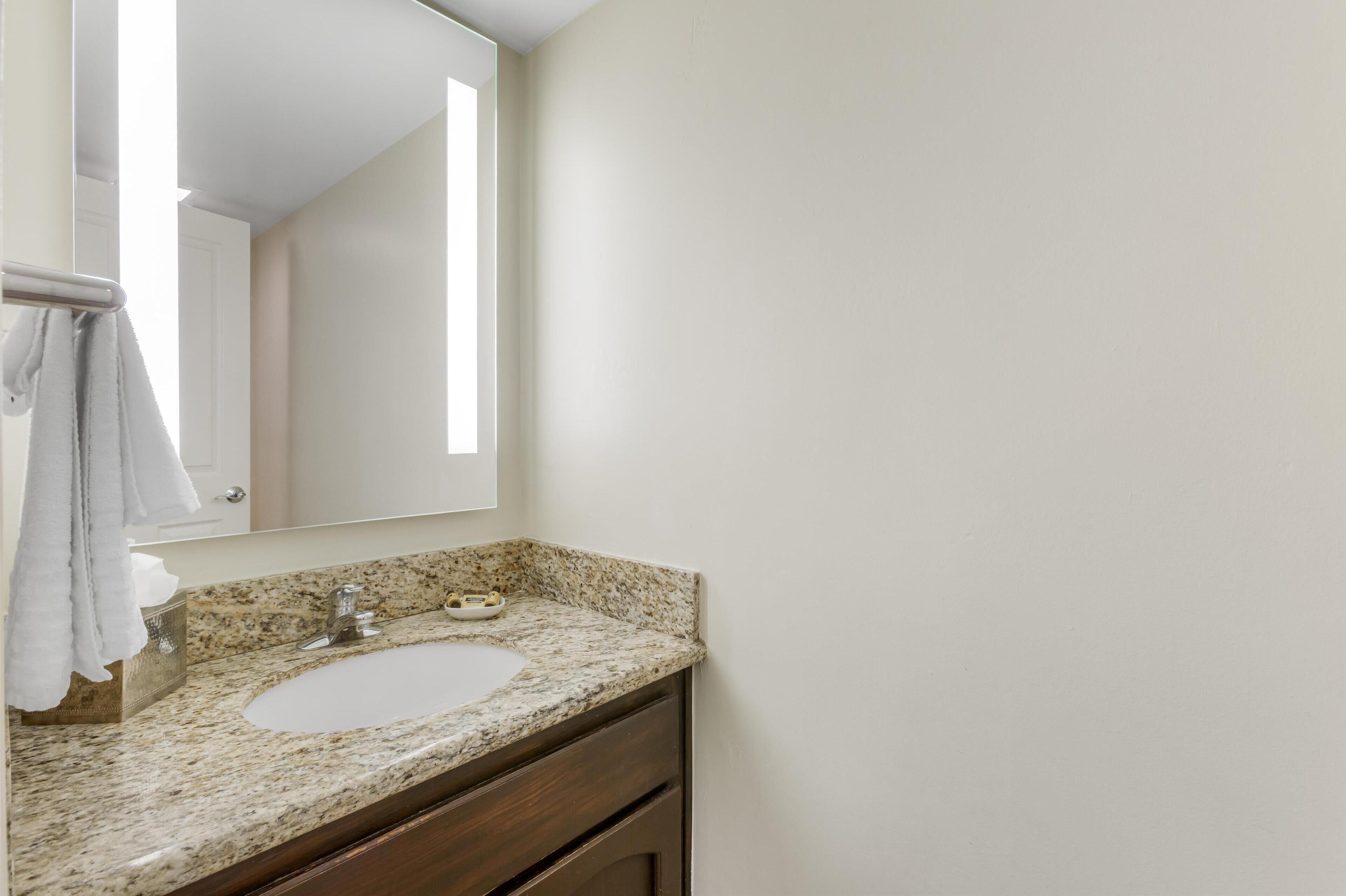 Une salle de bain avec un comptoir en granit, un lavabo blanc et un miroir.