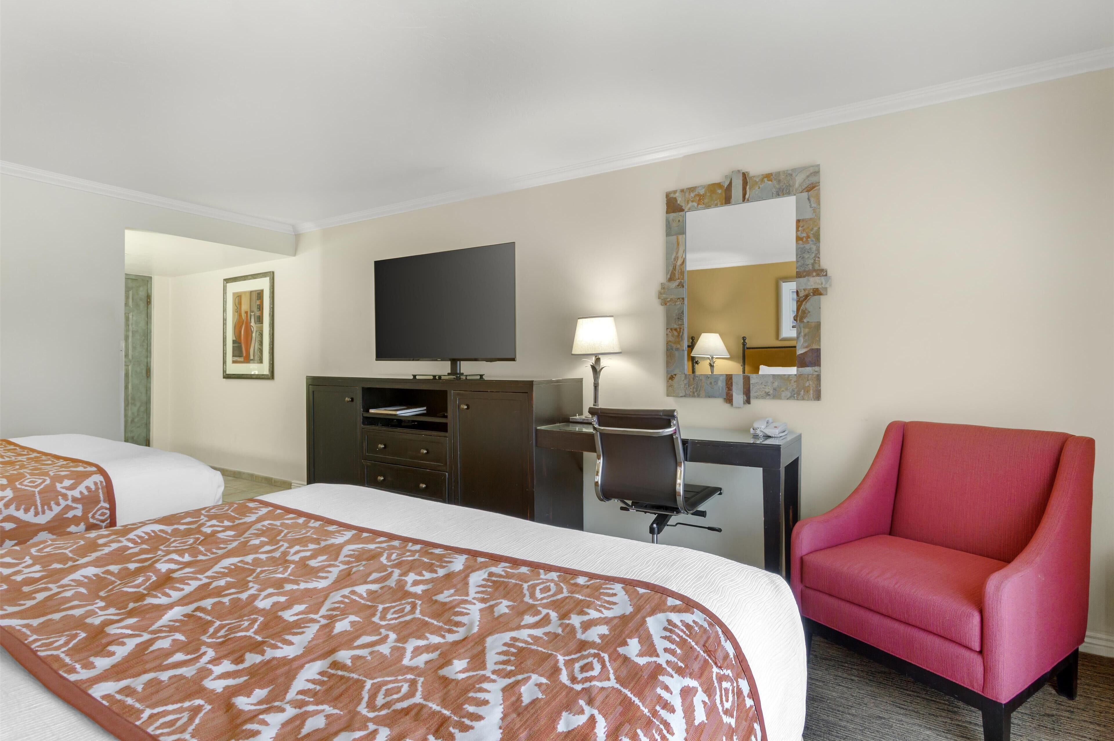 A hotel room with two beds, a desk, a chair, a television, and a mirror.