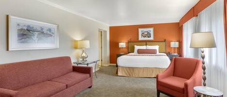 A hotel room with a bed, a red armchair, a small table, and a sofa.