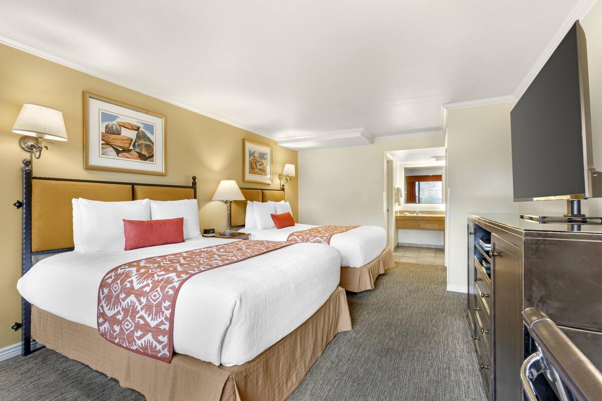 Une chambre d’hôtel avec deux lits, une télévision, un bureau et une salle de bain que l’on aperçoit à l’arrière-plan.
