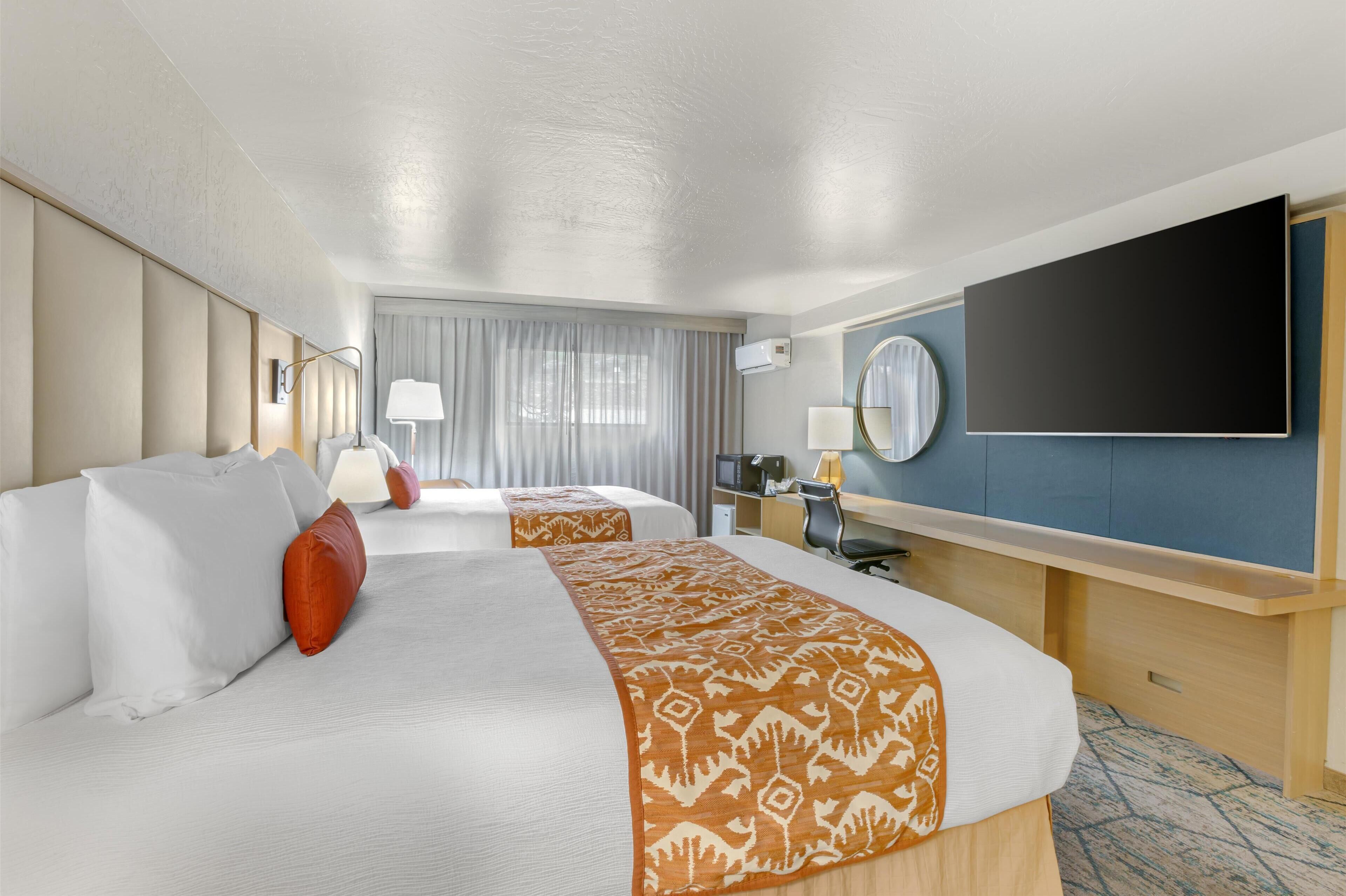 Une chambre d’hôtel avec deux lits, un bureau, une télévision et une grande fenêtre avec des rideaux.