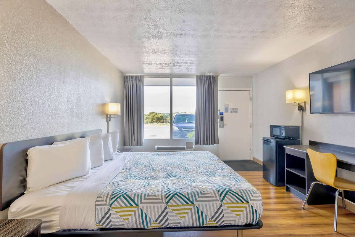 A hotel room with a bed, a desk, a chair, a TV, and a window with curtains.