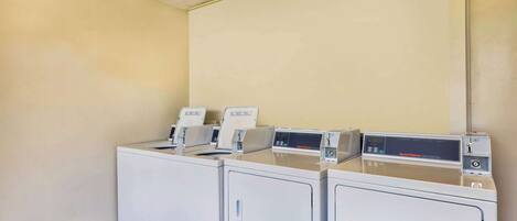 A laundry room with three stacked washing machines and dryers, a control panel, and a tiled floor.