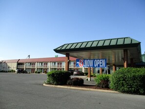 A motel with a 'NOW OPEN' sign, multiple rooms, and a parking lot.