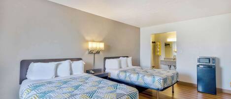 A hotel room with two beds, a small desk, a microwave, and a mirror.