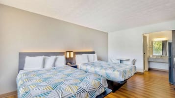 A hotel room with two beds, a wooden floor, a nightstand, and a bathroom visible through an open door.