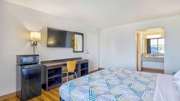 A hotel room with a bed, a desk with a chair, a small refrigerator, a microwave, a wall-mounted TV, and a window with a view.