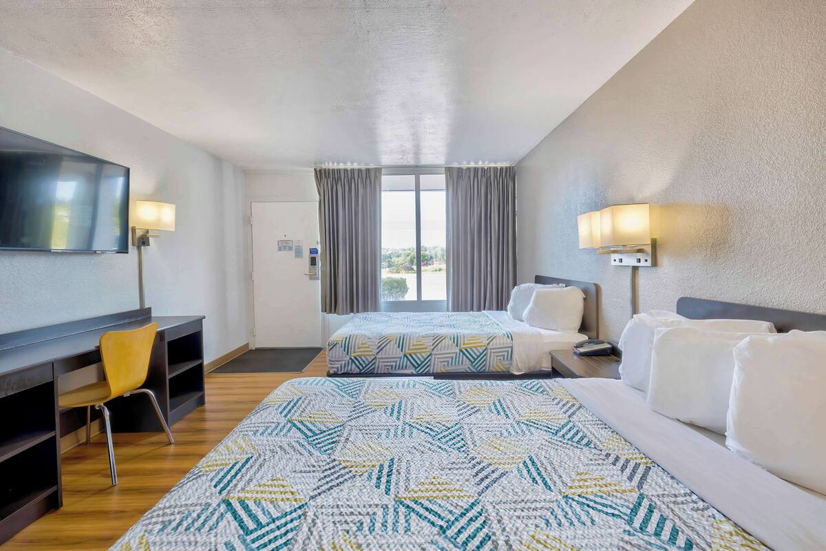 A hotel room with a bed, a desk, a chair, and a TV.