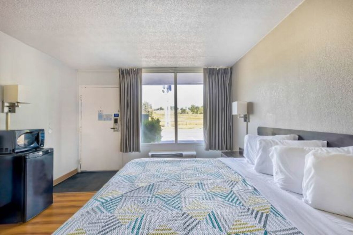 A hotel room with a bed, a desk with a microwave, a window with curtains, and a view of the outdoors.