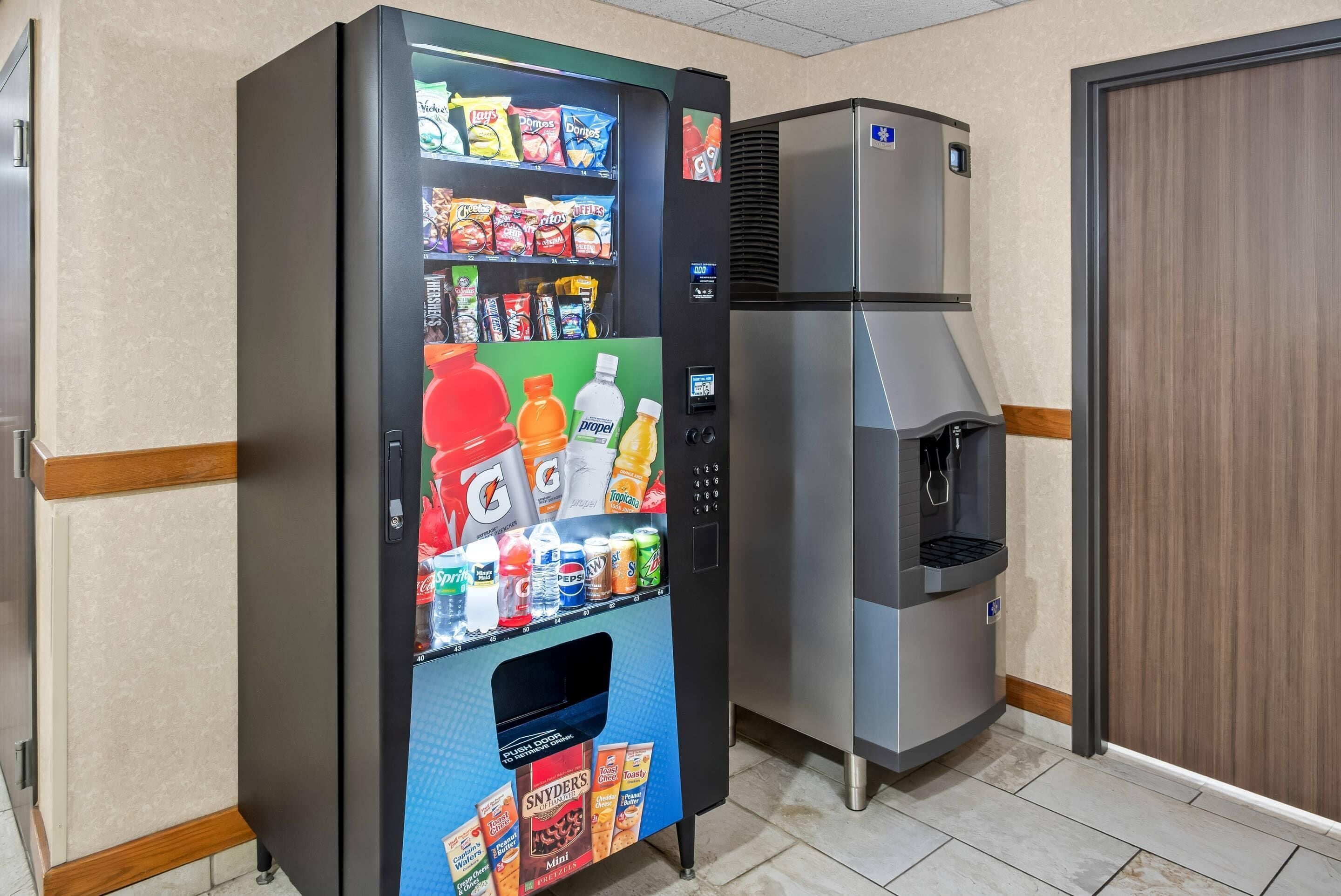 A vending machine with snacks and drinks, a water dispenser, and a refrigerator in a room with tiled flooring and wooden trim.