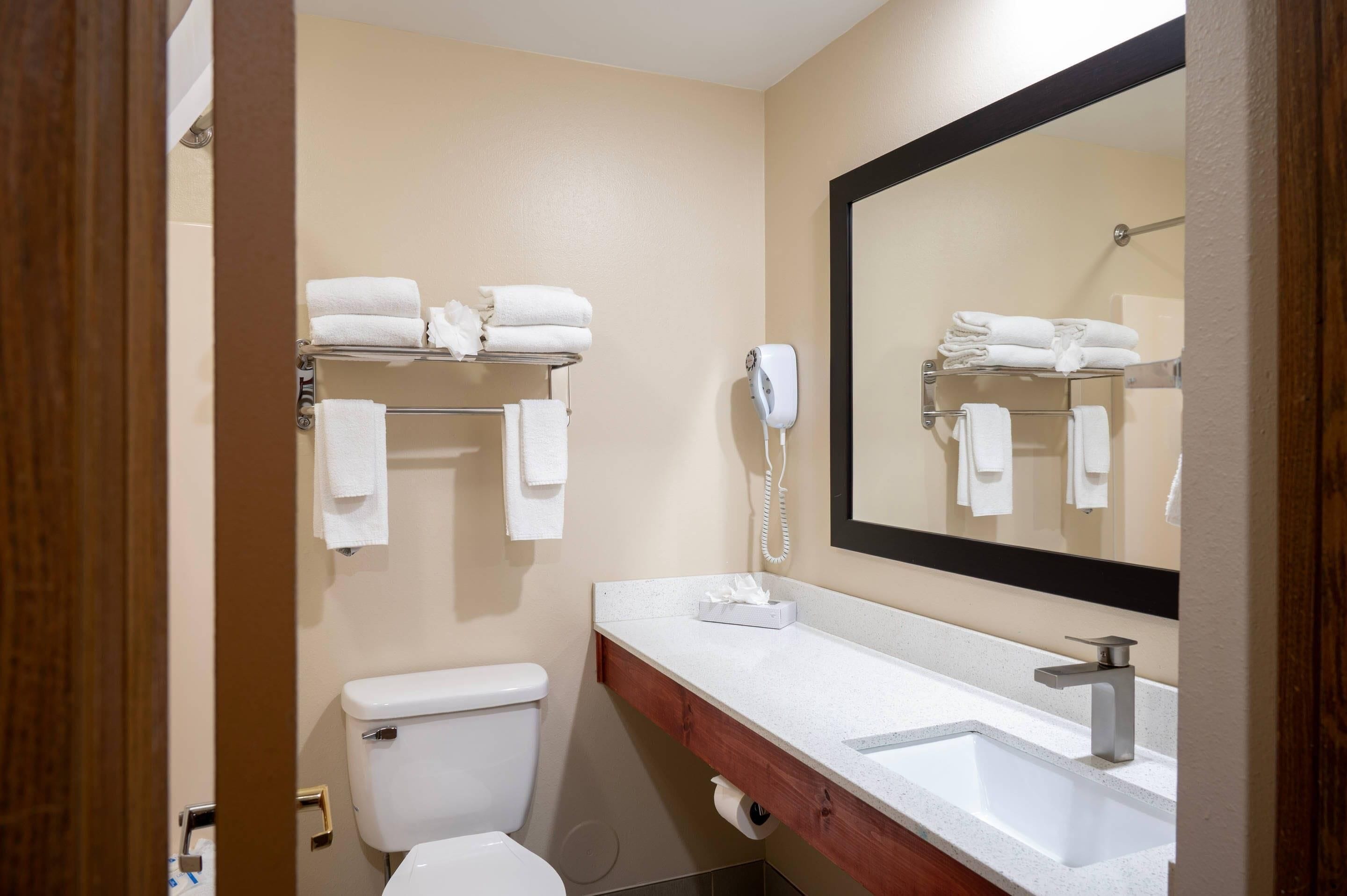A bathroom with a toilet, a sink, a mirror, and a towel rack with folded towels.
