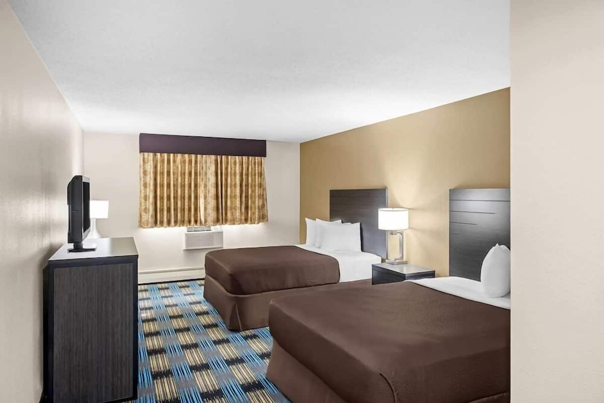 A hotel room with two beds, a desk, a TV, a window with curtains, and a patterned carpet.