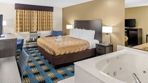 A hotel room with a king-sized bed, a sitting area with a desk and chair, a large bathtub, and a television.