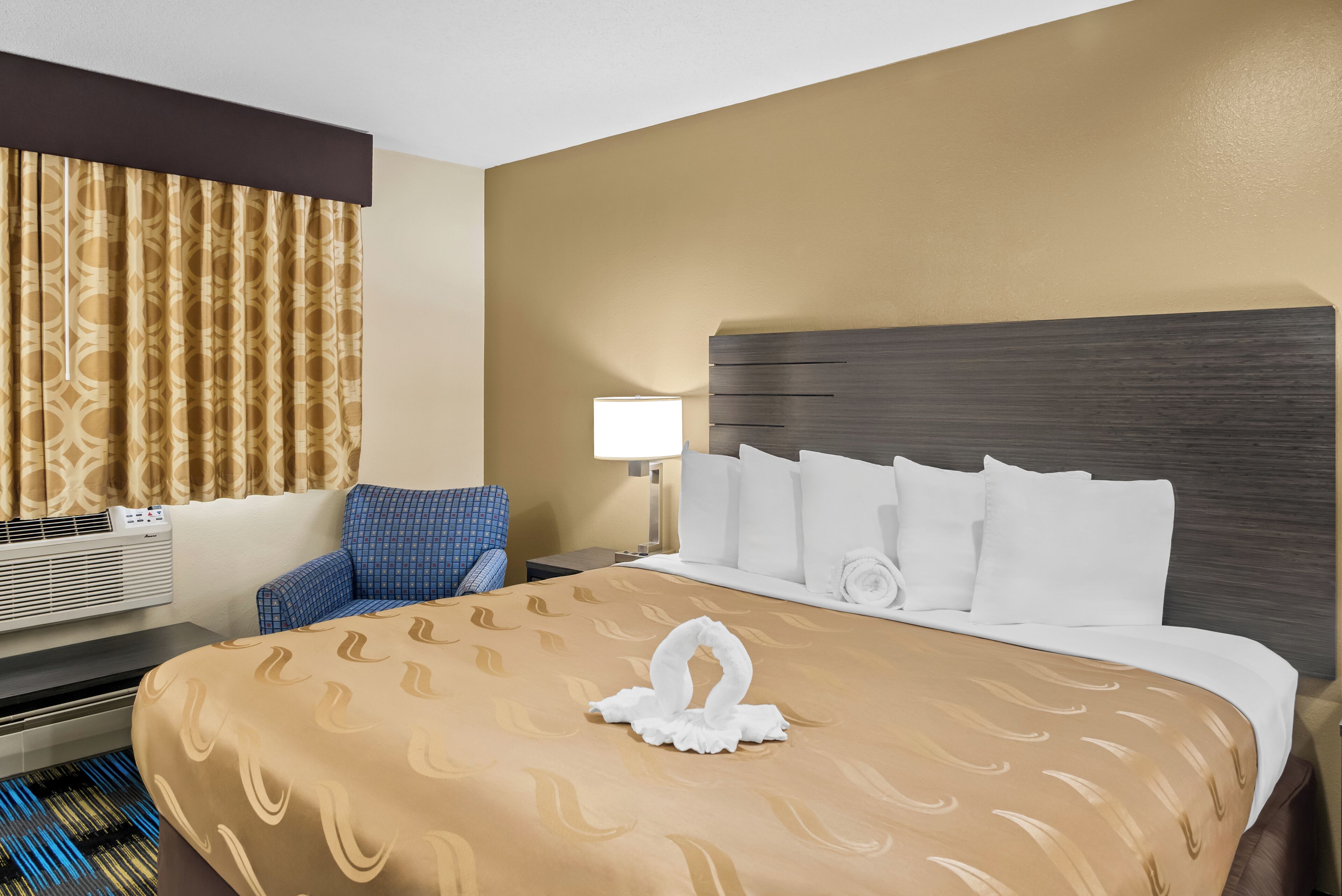 A hotel room with a large bed, a desk, a chair, a lamp, and a window with curtains.