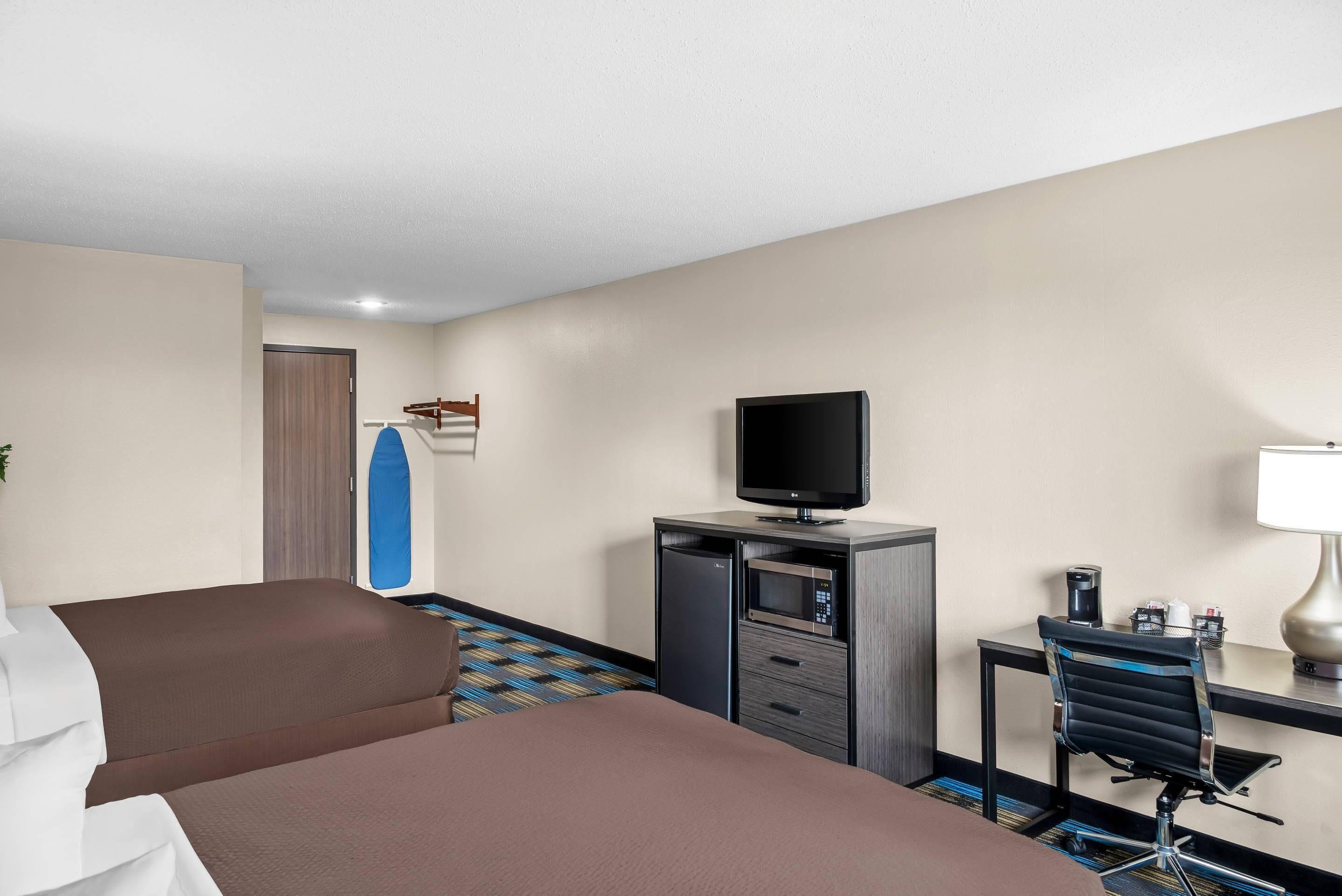 A hotel room with a bed, a desk with a computer, a television, and a small table with a lamp.