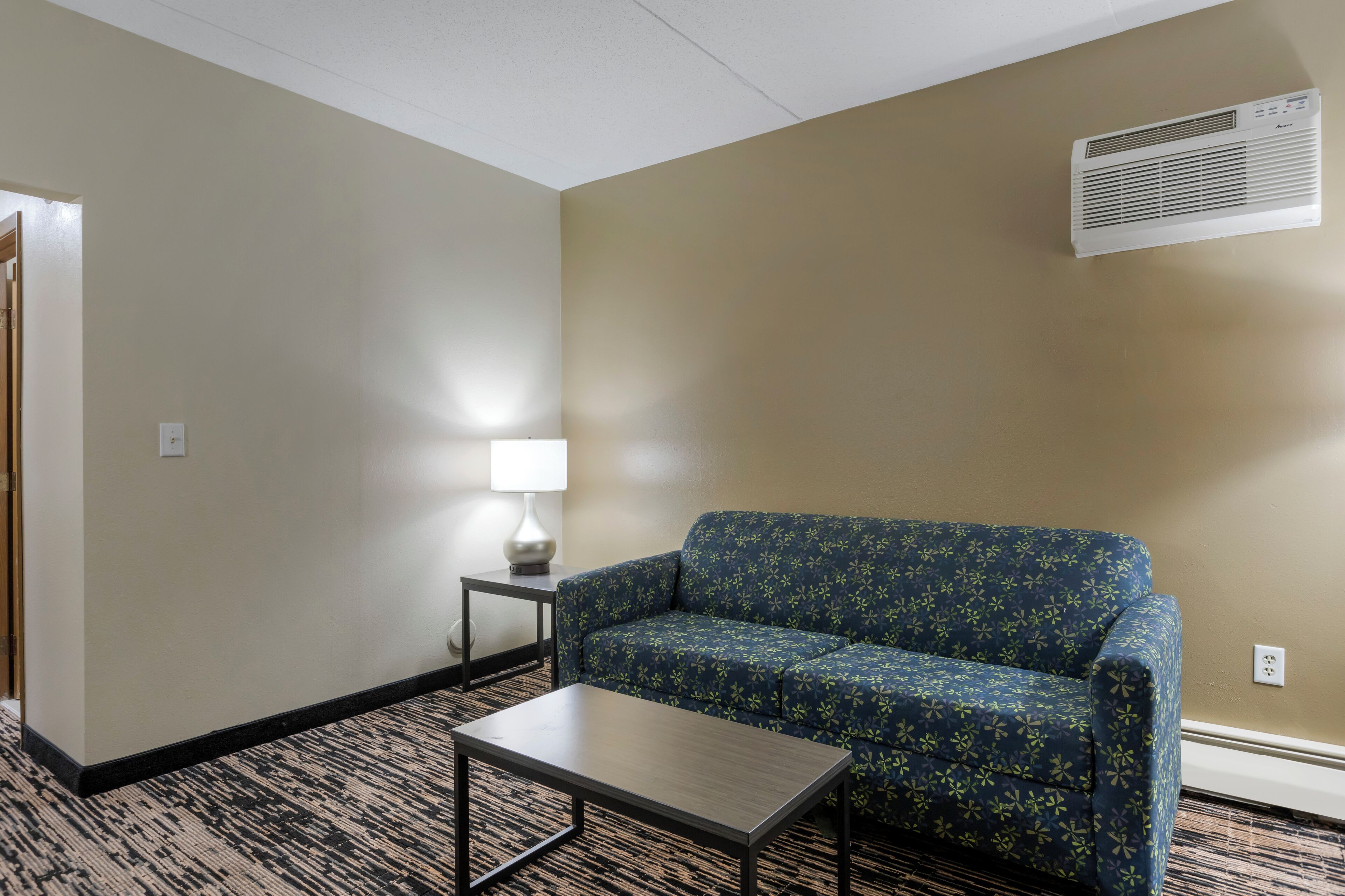 Una habitación de hotel con sofá, una mesita, una lámpara y un equipo de aire acondicionado.