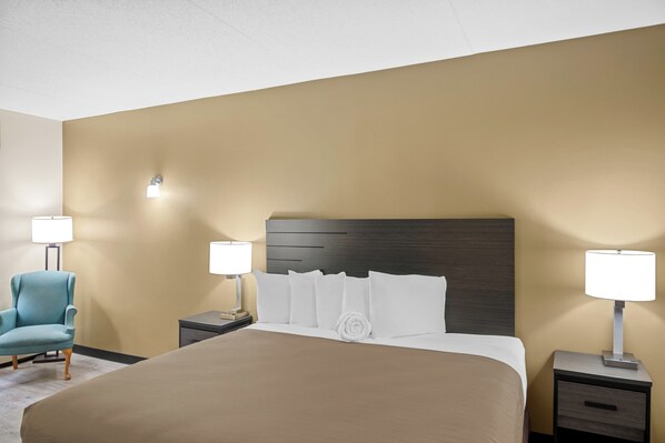 A hotel room with a large bed, two bedside tables with lamps, a chair, and a wall-mounted light fixture.