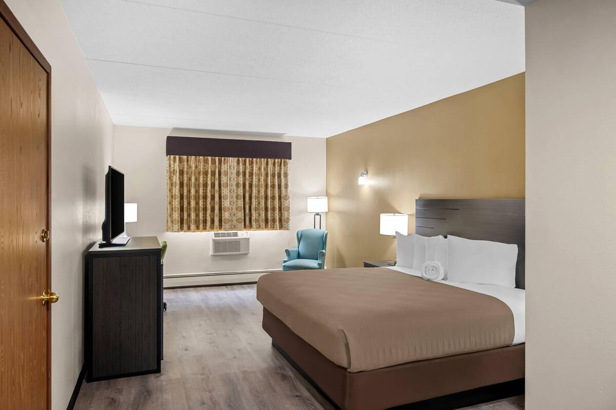 A hotel room with a bed, a desk, a chair, a TV, and a window with curtains.