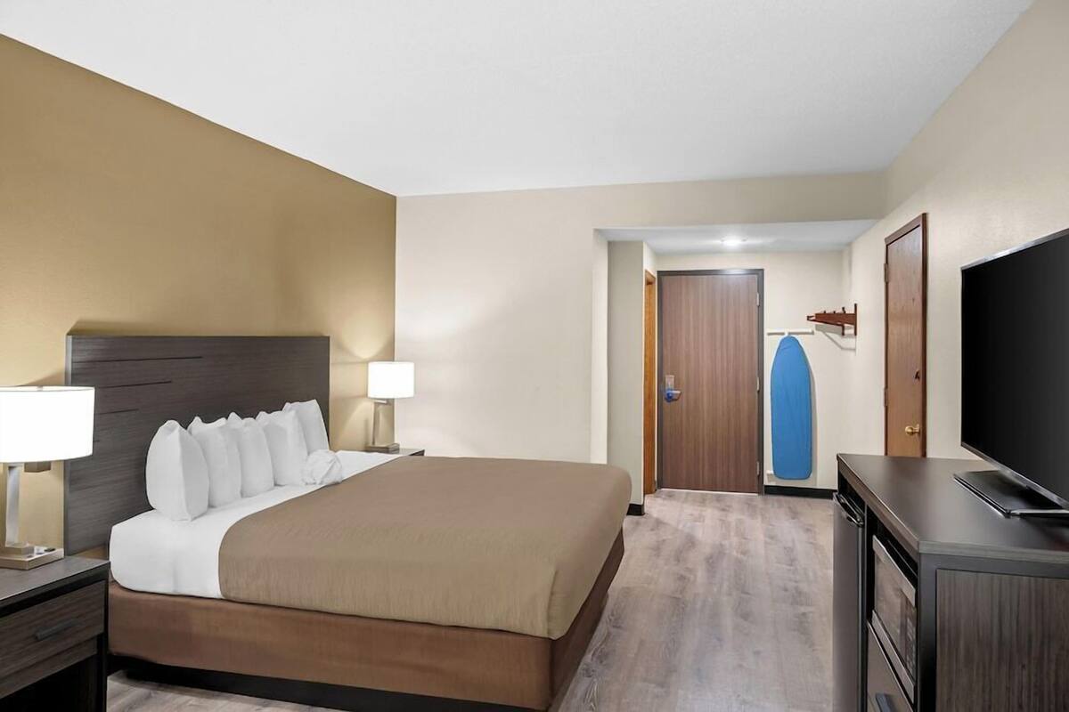 A hotel room with a bed, bedside lamps, a TV, a wardrobe, and a door leading to another room.