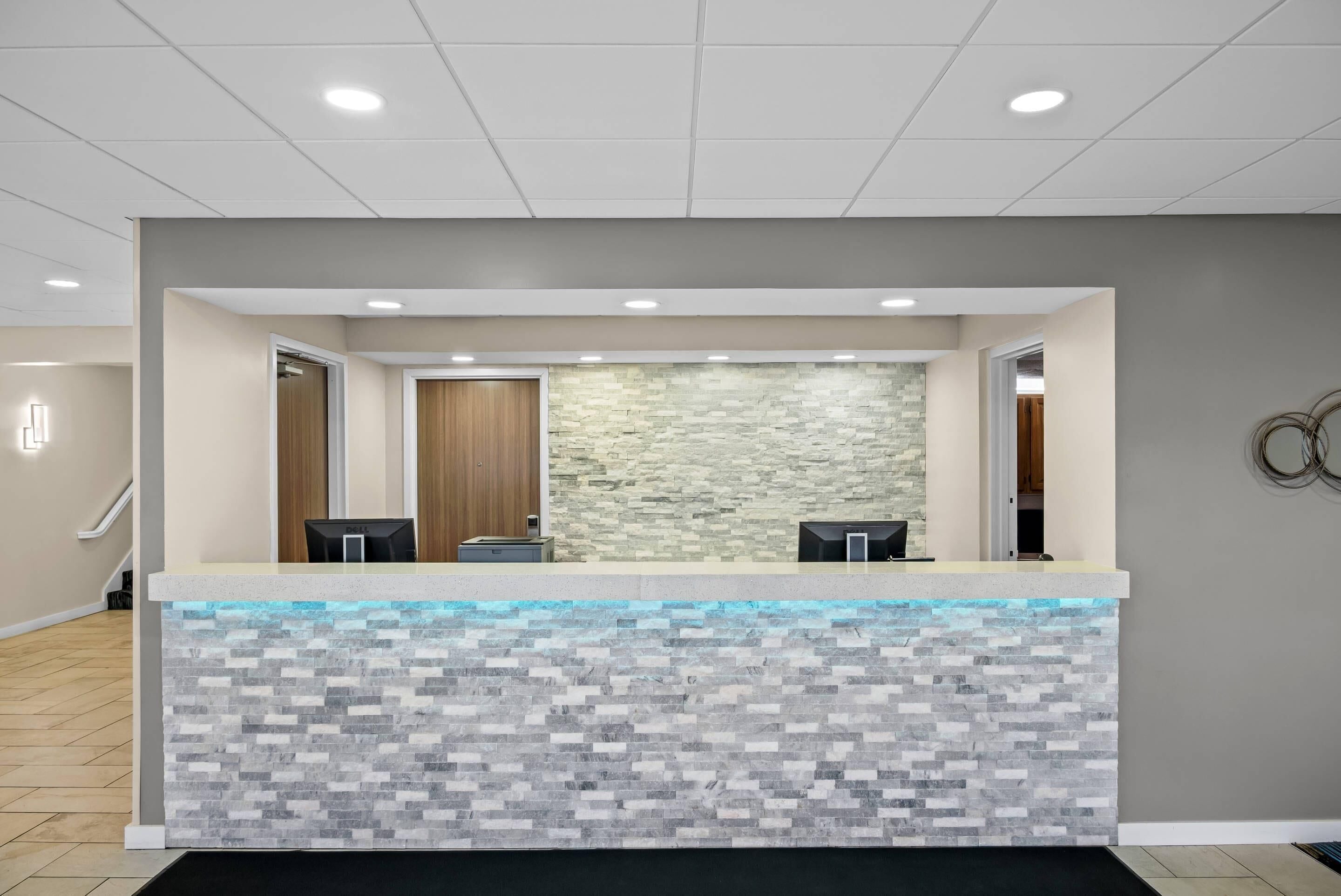 A reception area with a stone-textured counter, two black chairs, and a wooden door in the background.