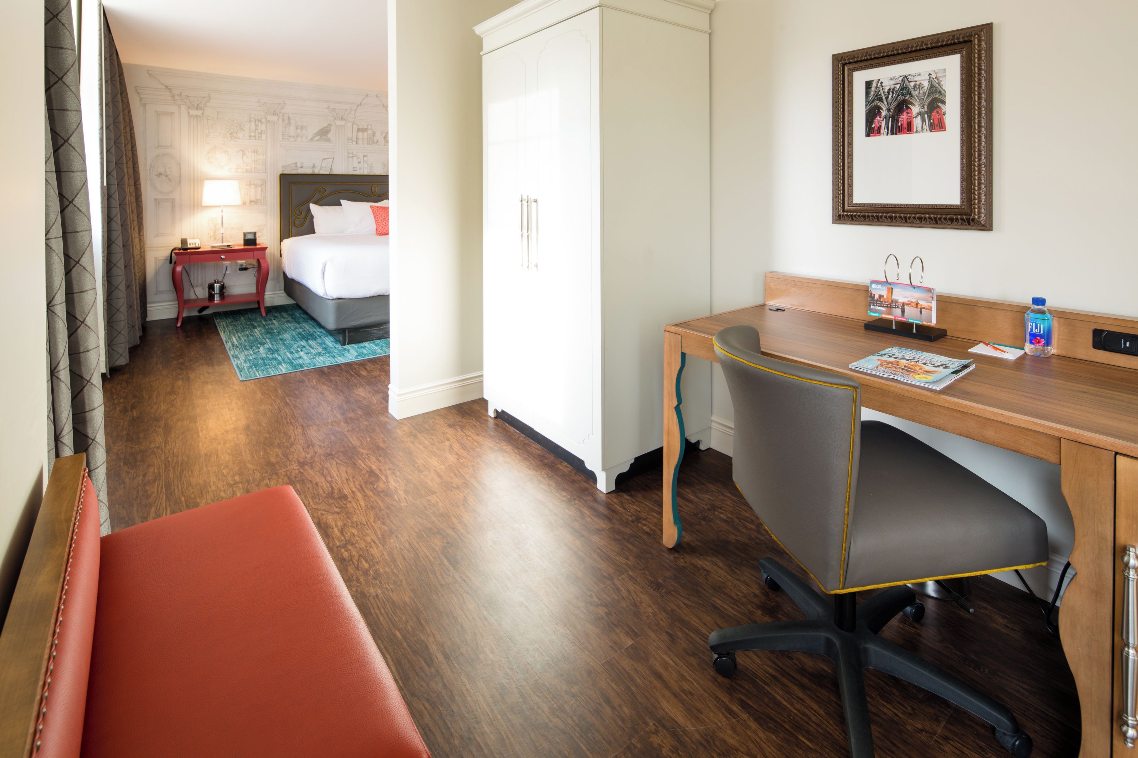 A hotel room with a bed, desk, chair, and a wardrobe.