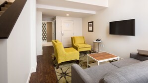 A modern living room with a staircase, a flat-screen TV mounted on the wall, and two armchairs. - Hotel Indigo Baltimore Downtown by IHG (Baltimore)