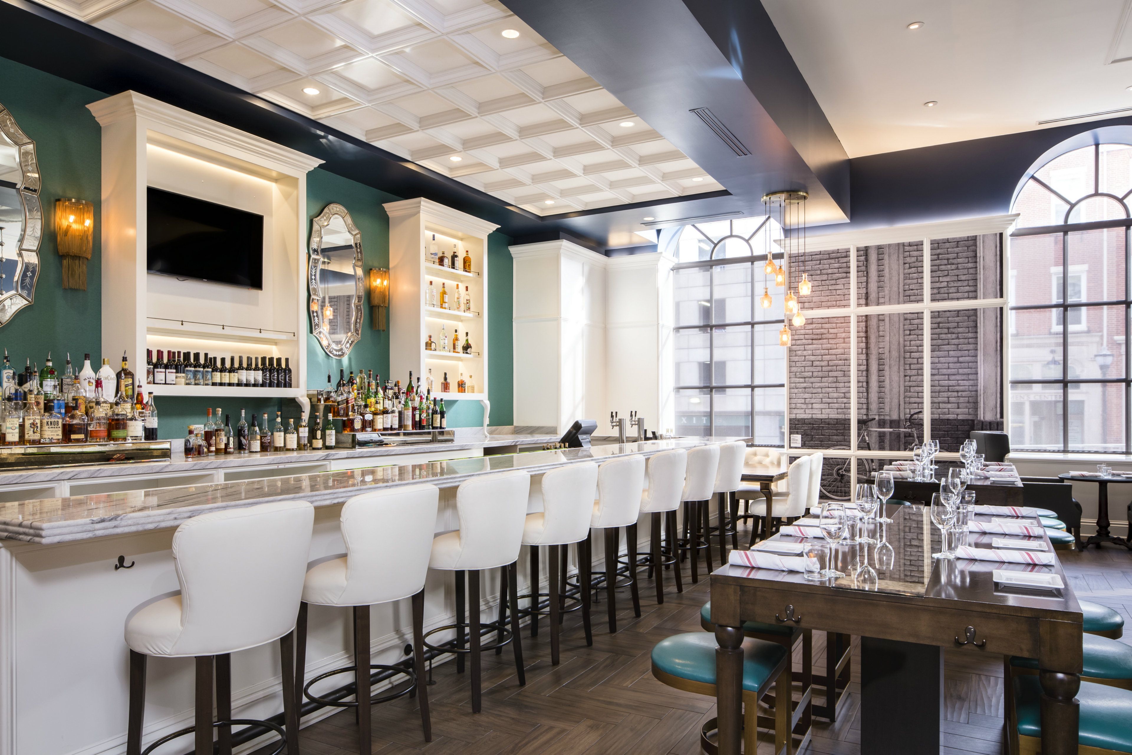 A bar area with a long counter, multiple stools, and a variety of bottles.