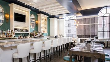 A bar area with a long counter, multiple stools, and a variety of bottles.