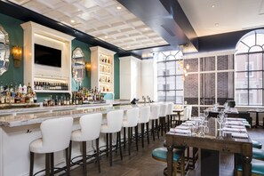 A bar area with a long counter, multiple stools, and a variety of bottles. - Hotel Indigo Baltimore Downtown by IHG (Baltimore)