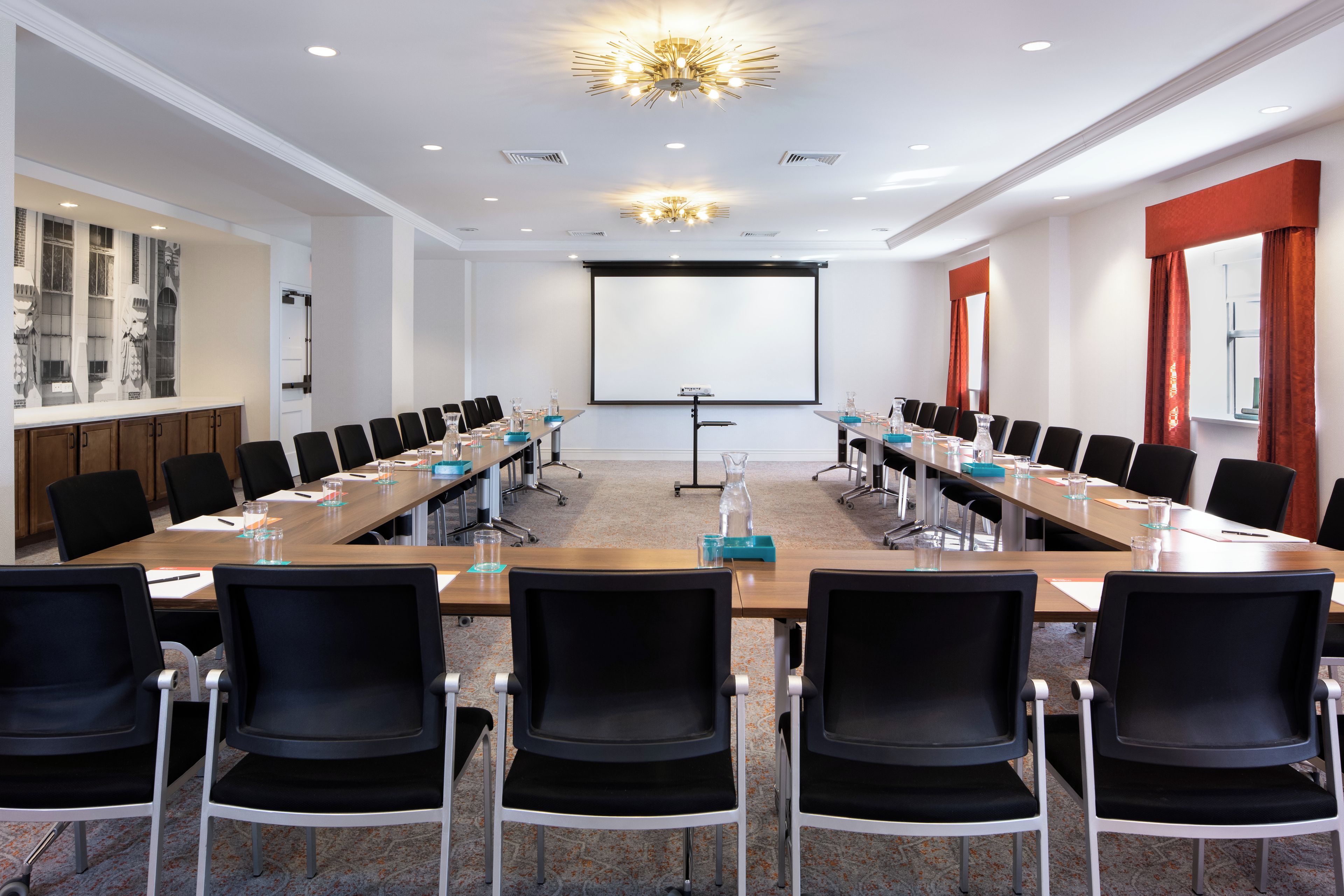 Une salle de conférence avec une longue table, des chaises noires et un écran de projection.