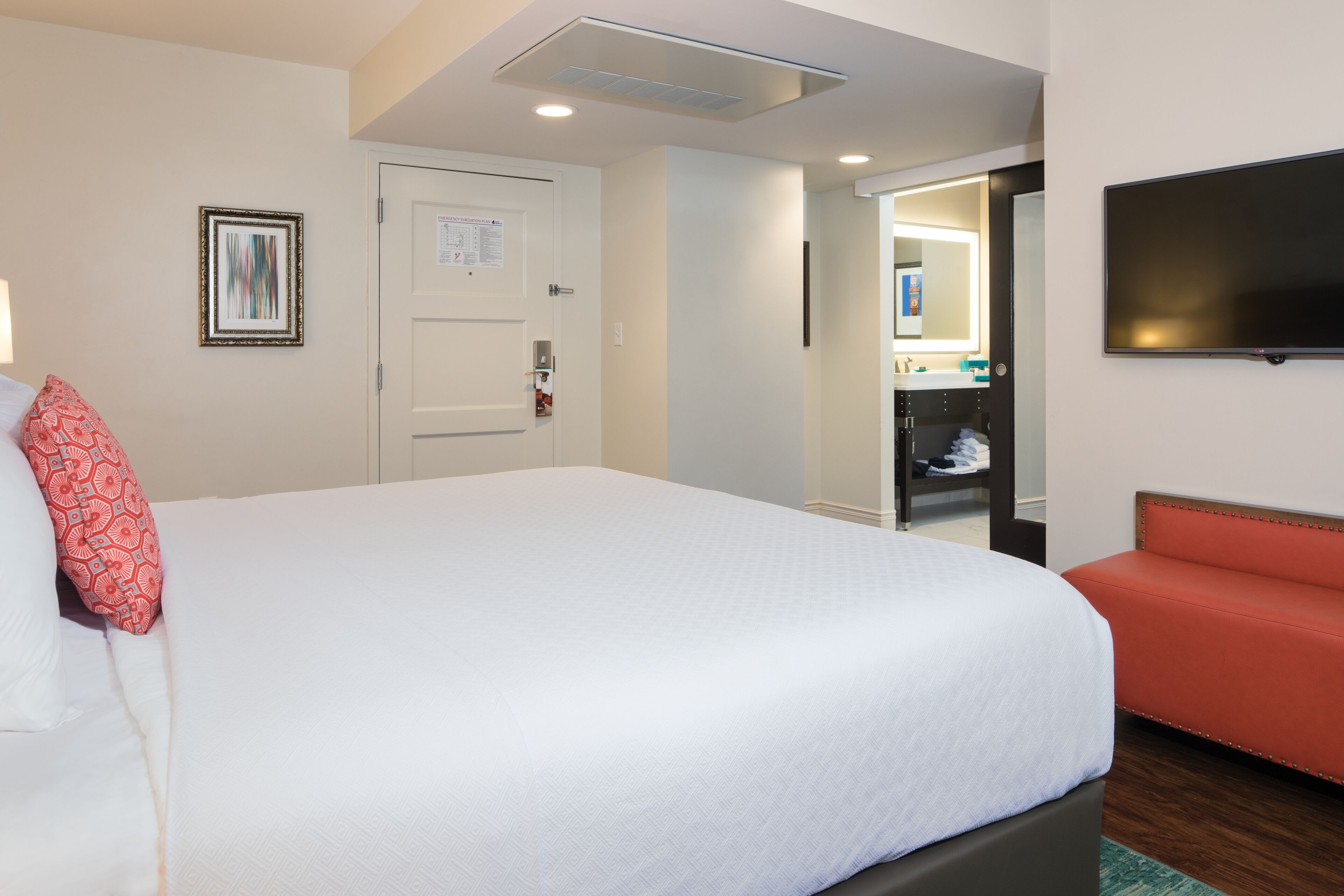 A hotel room with a large bed, a red sofa, a TV mounted on the wall, and a door leading to a bathroom.